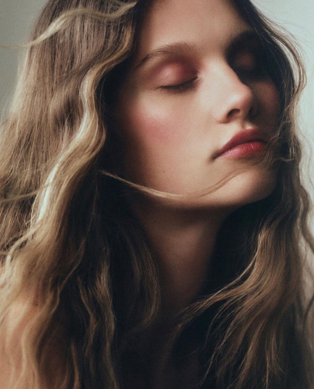 Close up portrait of a young woman with wavy brown hair and closed eyes with soft natural makeup in Los Angeles