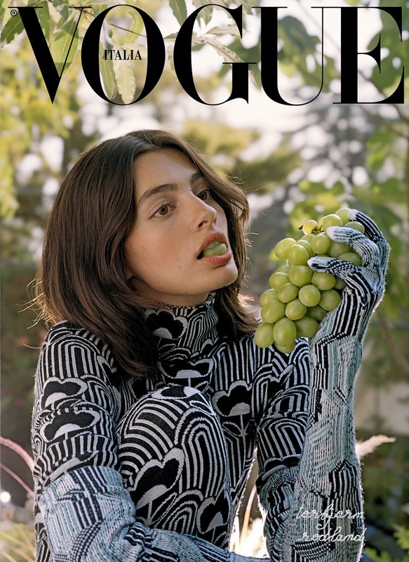 Vogue Italia cover featuring a woman in a patterned turtleneck and gloves eating grapes outdoors, framed by green leaves.