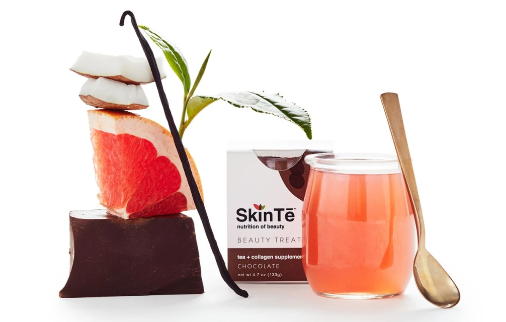 Still life composition featuring chocolate, grapefruit, coconut, tea leaf, vanilla bean, and SkinTe chocolate collagen beauty supplement drink.