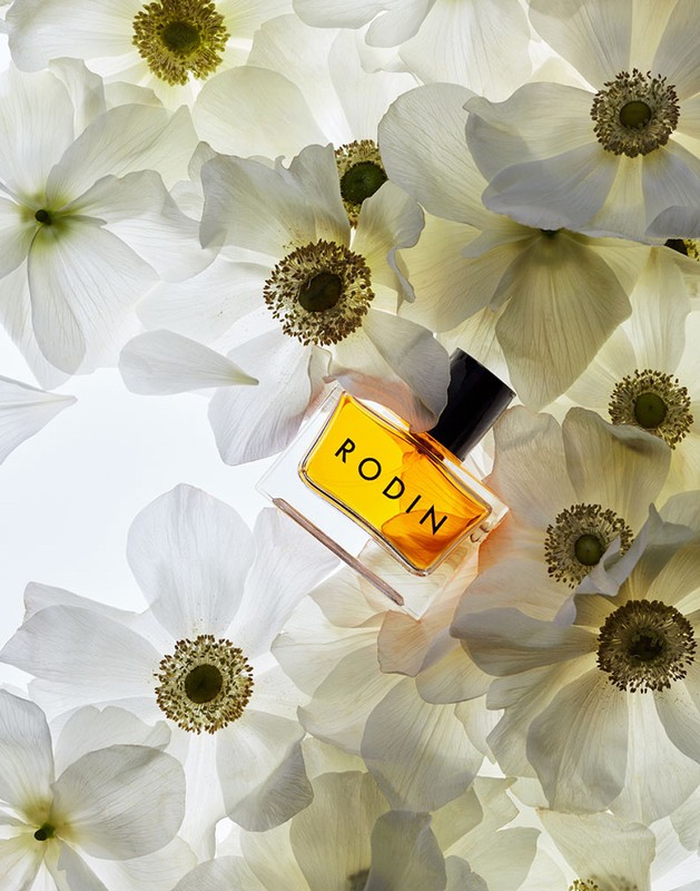 Rodin perfume bottle rests on a bed of white anemone flowers, with a high-angle view emphasizing the elegance and floral theme.