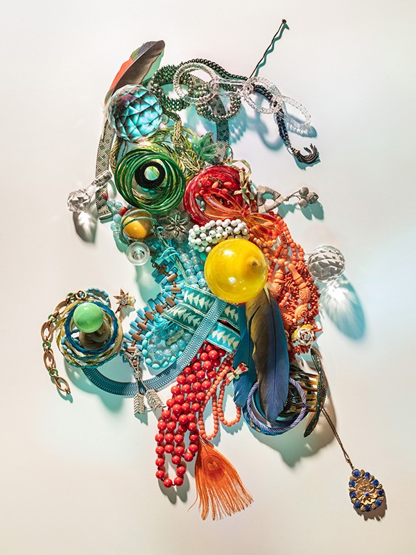 Colorful beads, baubles, and jewelry arranged as a unique, abstract design on white. Decorative objects including feathers and crystals.