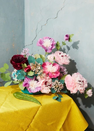 Still life photography of a vibrant floral arrangement with pink and red flowers in a turquoise vase on a yellow tablecloth.