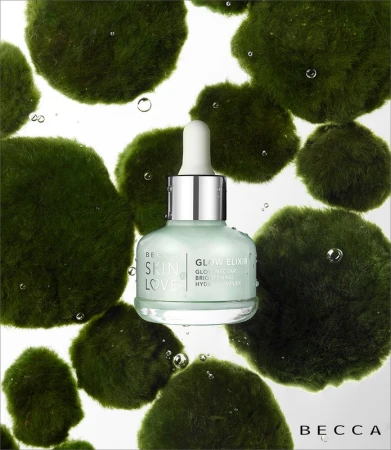 Becca Glow Elixir skincare bottle surrounded by green moss spheres against a white background