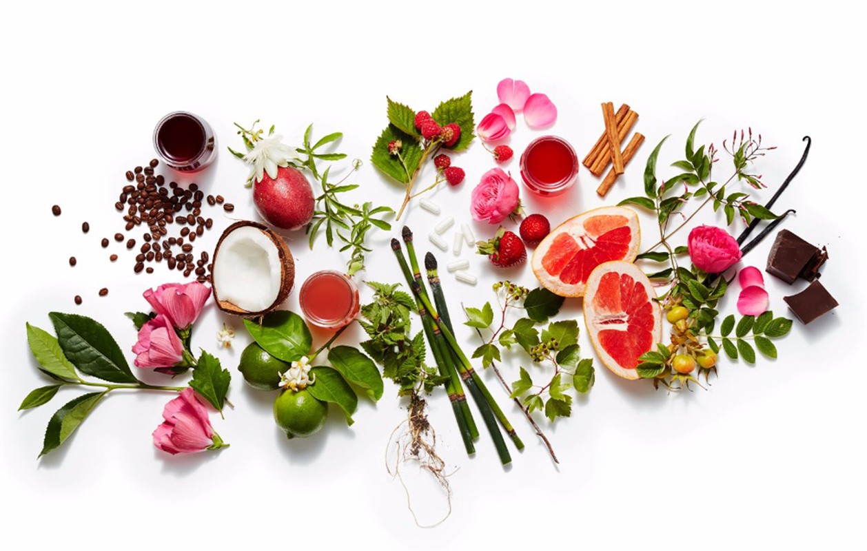 Still life featuring colorful array of fruits, flowers, herbs, spices, and liquids on a white backdrop, creating a vibrant mix.