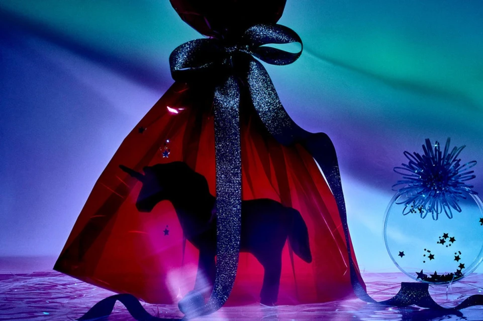 Unicorn figurine inside a transparent gift bag tied with a black ribbon, accented by stars, with a blue decorative sphere.