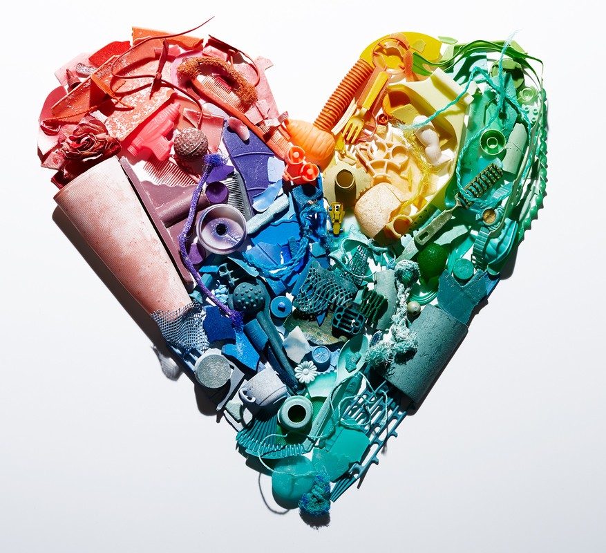 Colorful heart shape made from plastic trash and debris, arranged on a white background. Environmentalism and recycling concept.