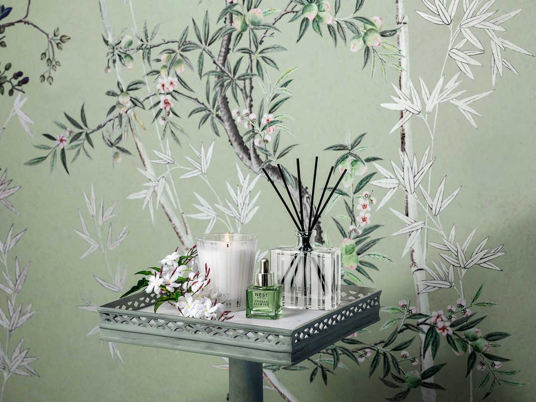 Interior setting with a fragrance diffuser, candle, and perfume on a tray, with floral and bamboo wallpaper in the background.