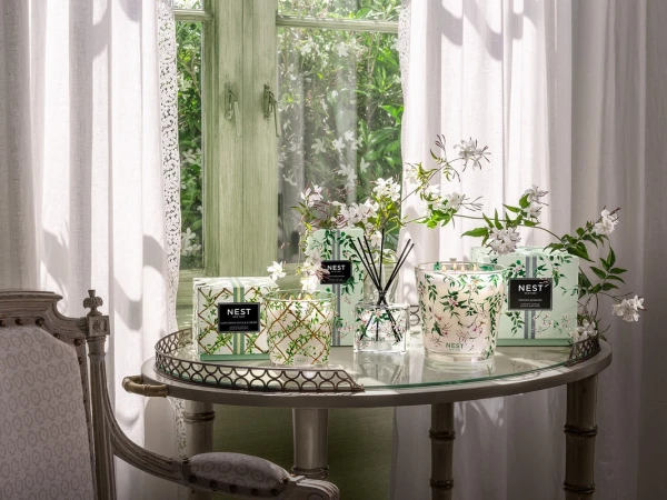 Elegant display of NEST New York home fragrance products on a glass table next to a window with white curtains, creating a fresh ambiance.