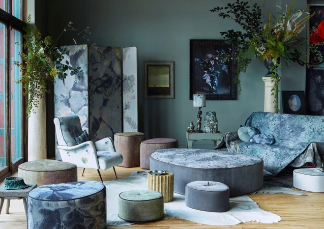 Eclectic living room interior with round upholstered furniture, patterned textiles, and floral arrangements against a muted teal wall.