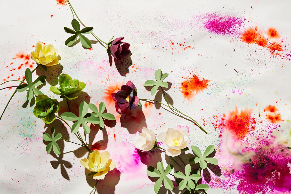Artistic flat lay with paper flowers in yellow, green, burgundy and white, complemented by paint splatters in red, pink and turquoise.