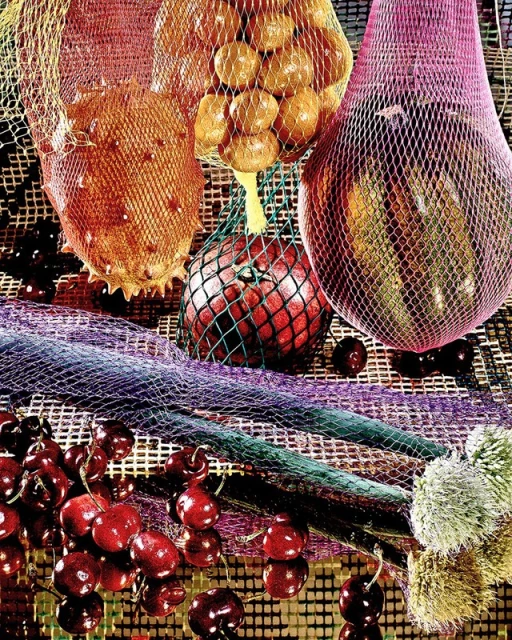 Still life composition with kiwano melons, plums, cherries, and apples in colorful mesh bags creating a vibrant, textured visual.