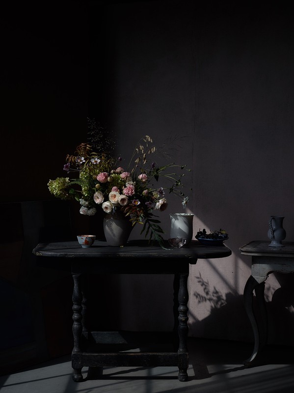 A lush floral arrangement in a ceramic vase on a dark wooden table with dramatic chiaroscuro lighting.