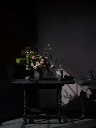 A lush floral arrangement in a ceramic vase on a dark wooden table with dramatic chiaroscuro lighting.