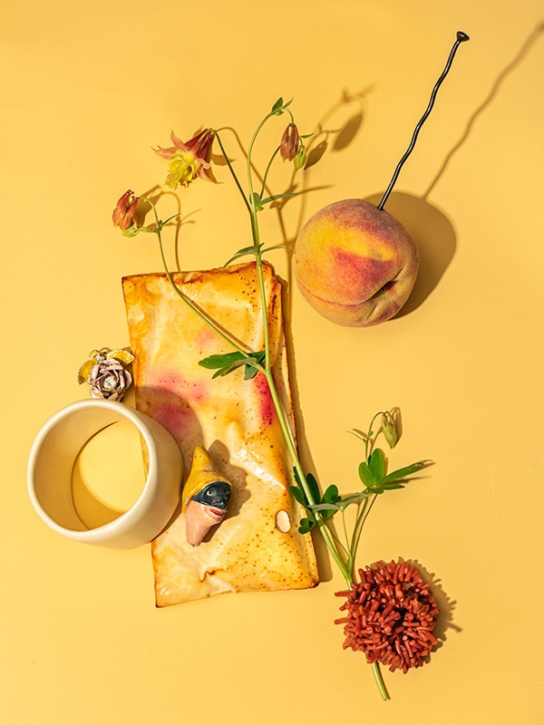 Still life of a peach, flowers, ceramic bowl, and paper on a yellow background with shadows, suitable for food and art photography.