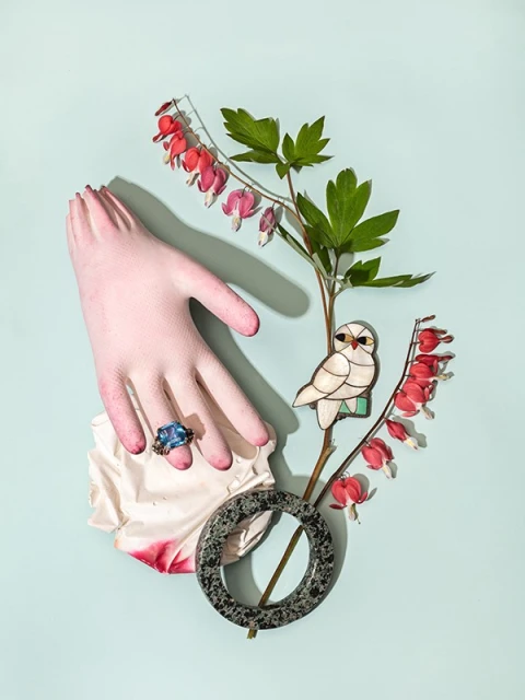 Mannequin hand displays an aquamarine ring with bleeding heart flowers, an owl brooch, and a marble ring on a light blue background.