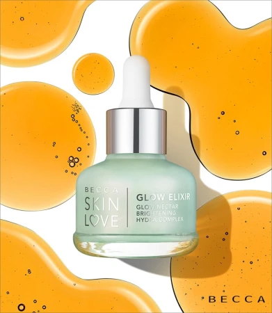 Close-up of BECCA Skin Love Glow Elixir bottle on white, surrounded by viscous orange liquid. Beauty, skincare, and product photography.
