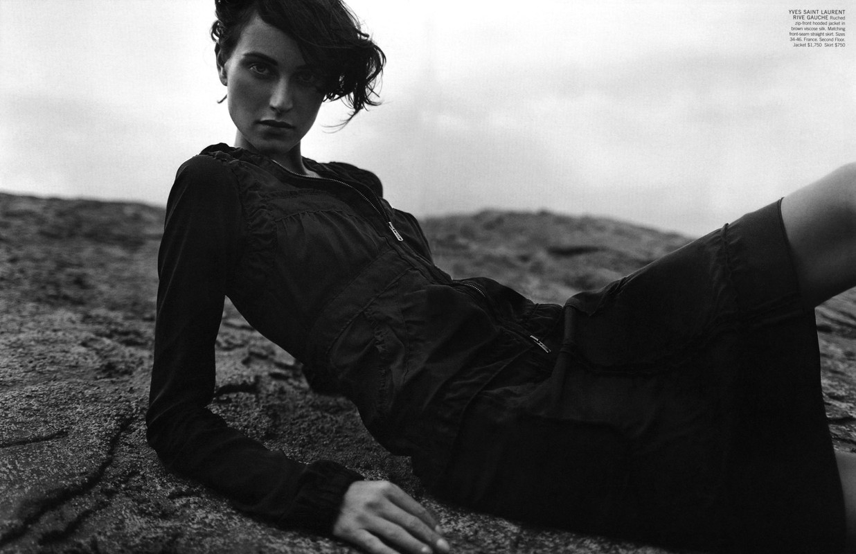 Model lying on rocky terrain wearing a dark zip-top hooded jacket and skirt styled by Lorri Sendel