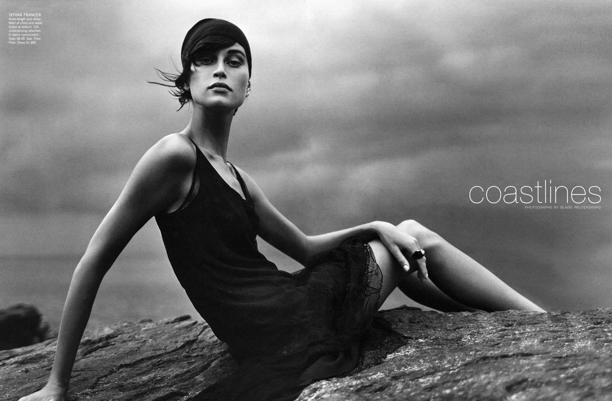 Monochrome fashion shot of a woman in a flapper-style dress sitting on rocks, set against a cloudy sky with coastlines text overlay.