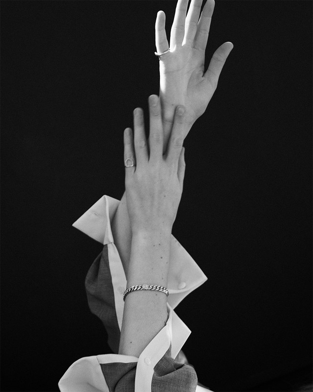 Elegant black and white image featuring a person's arms and hands adorned with rings and a bracelet, set against a dark background.