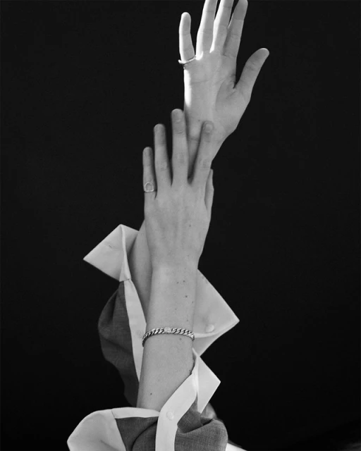 Elegant black and white image featuring a person's arms and hands adorned with rings and a bracelet, set against a dark background.