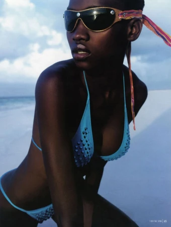 Model wearing a blue bikini and tinted futuristic sunglasses with colourful straps against a beach backdrop.