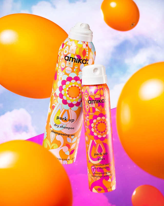 Two Amika dry shampoo cans stand out against a vibrant background with orange spheres. Cosmetic product shot for hair care and styling.