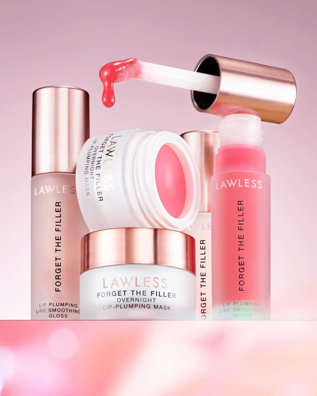 Cosmetic still life on a pink background featuring Lawless Forget The Filler lip-plumping gloss and overnight lip-plumping mask containers.