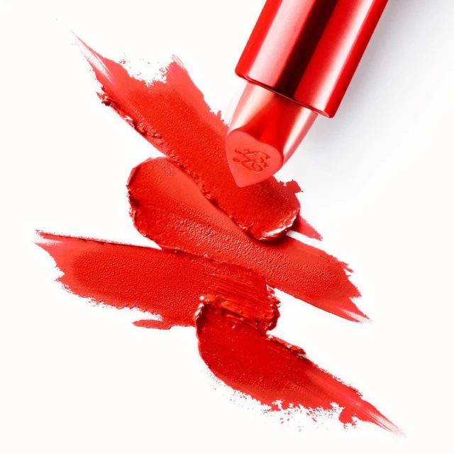 Close-up of a red lipstick tube with swipes of red lipstick on a white background, showcasing beauty and cosmetic products.