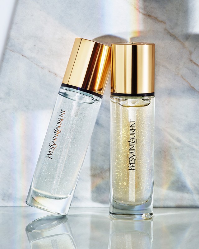 Two YSL beauty serum bottles, one upright and one leaning, feature clear glass, gold caps, and prominent YVES SAINT LAURENT branding.