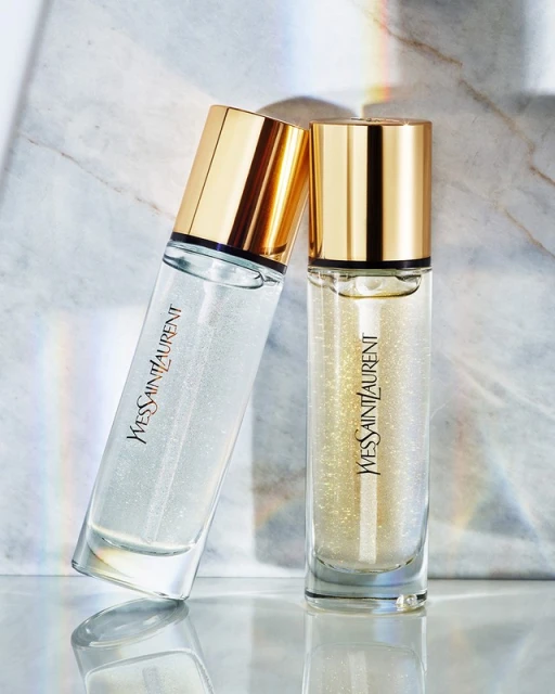 Two YSL beauty serum bottles, one upright and one leaning, feature clear glass, gold caps, and prominent YVES SAINT LAURENT branding.