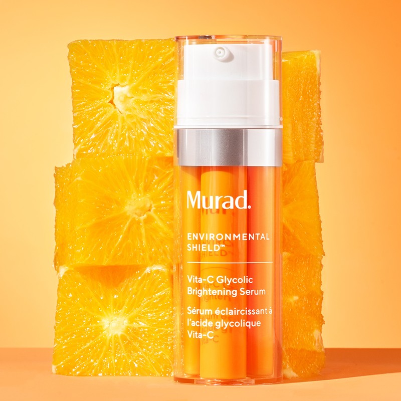 Murad Vita-C Glycolic Brightening Serum bottle surrounded by orange slices against an orange background, beauty shot.