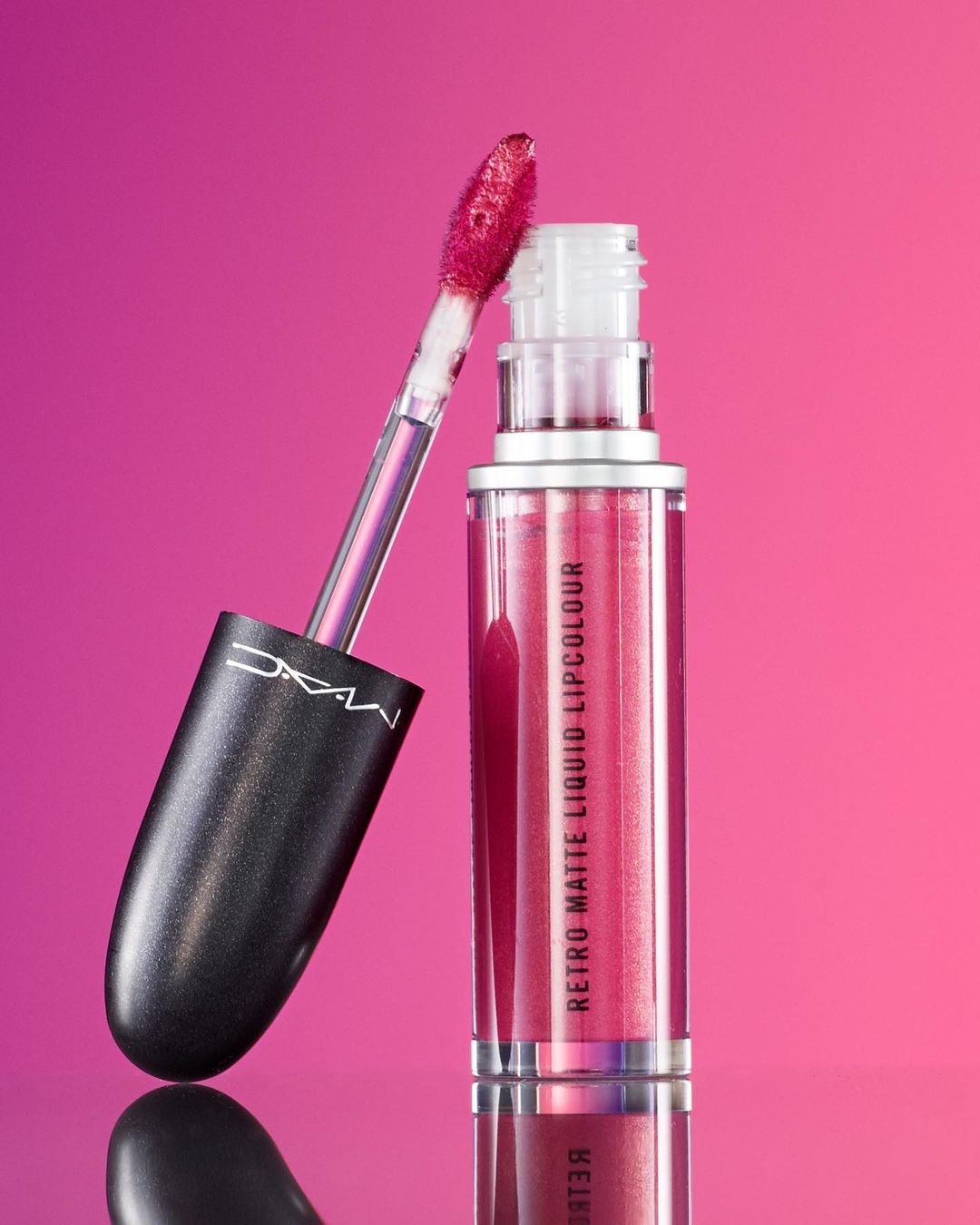 MAC Retro Matte Liquid Lipcolour in a clear container with black handle and applicator, against a pink to magenta gradient background.