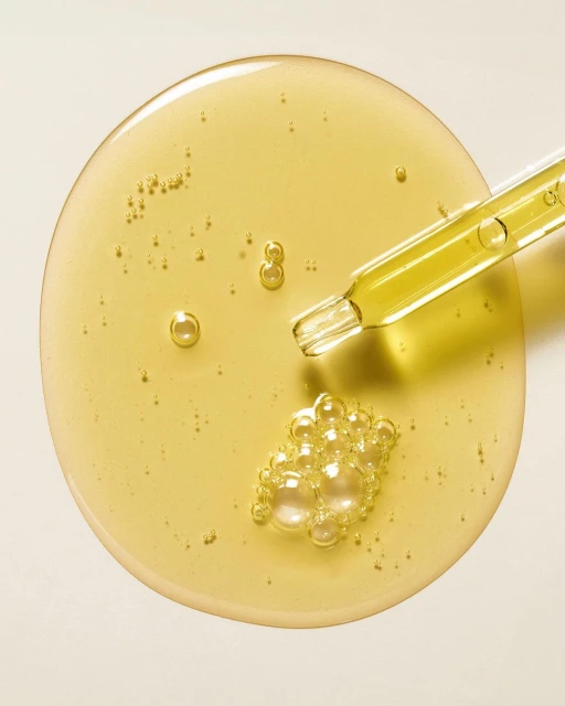 Overhead shot of cosmetic serum with bubbles and a pipette on an off-white background, showcasing texture and product consistency.