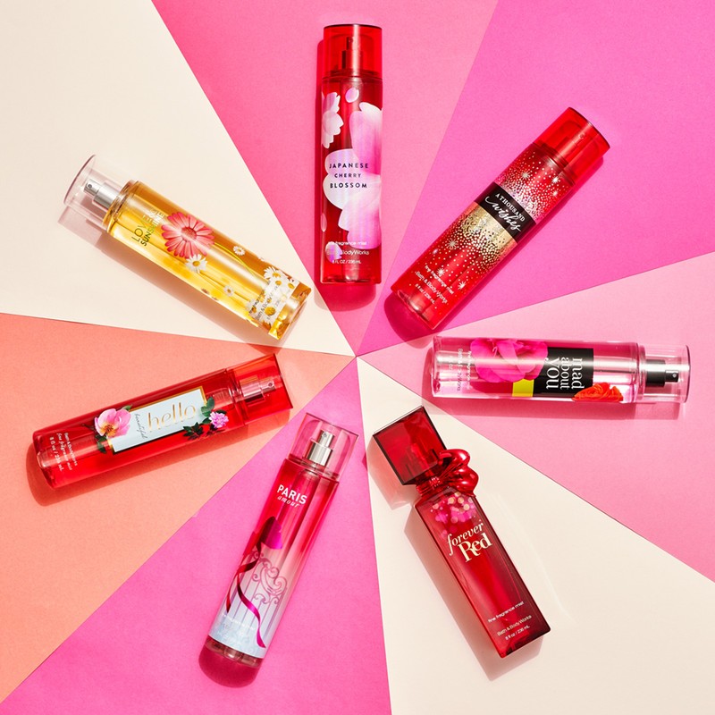 Arrangement of various Bath & Body Works fragrance mist bottles in an eye-catching circle against a bright pink and white background.