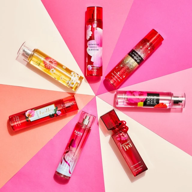 Arrangement of various Bath & Body Works fragrance mist bottles in an eye-catching circle against a bright pink and white background.