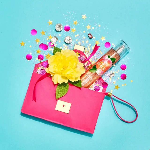 Flat lay photo of a bright pink purse with a yellow flower, bottle of body mist, and confetti on a blue background.