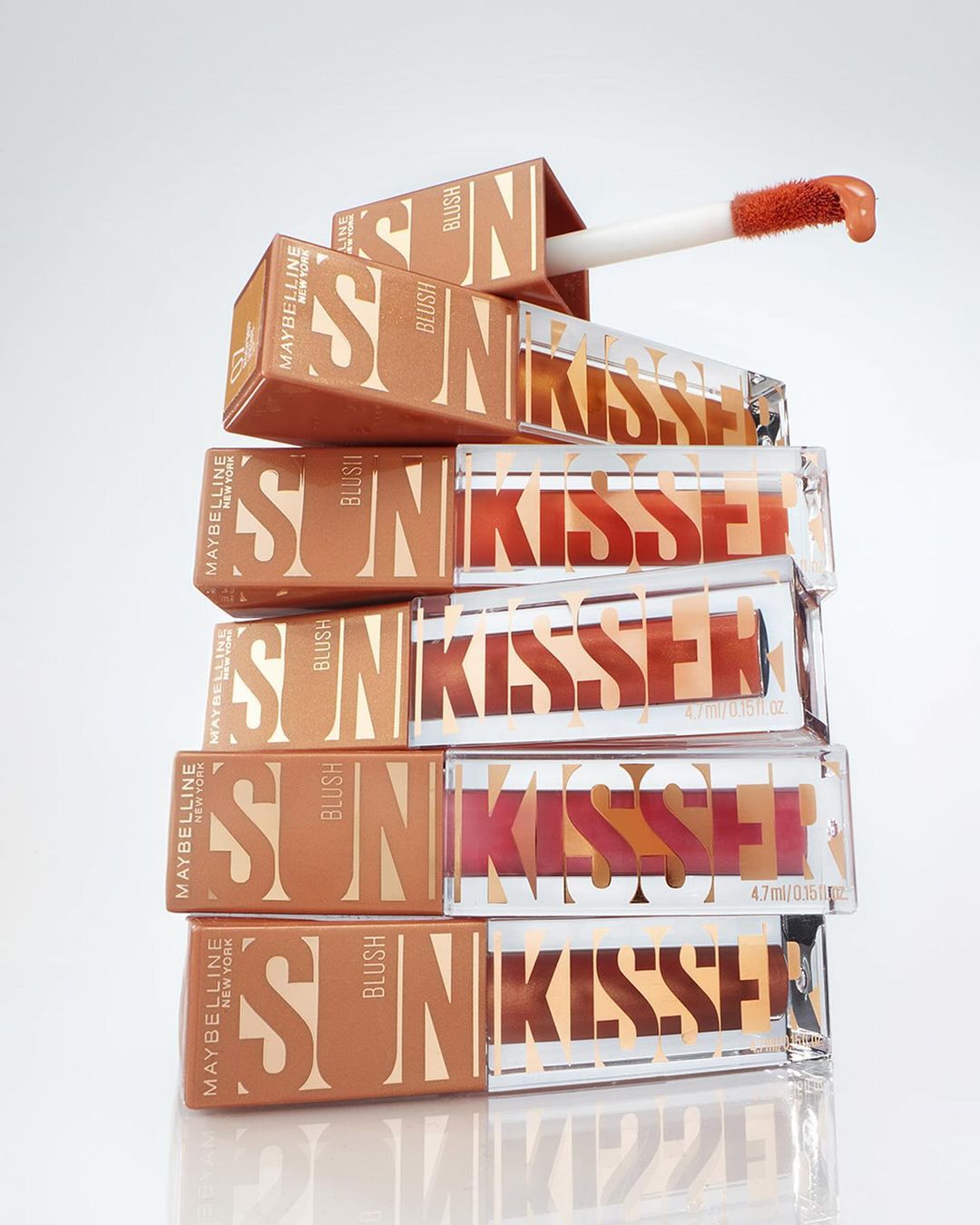 Stack of Maybelline Sun-Kissed Blush product packaging, featuring blush compacts with applicator wands, bronze and clear containers, studio lighting.