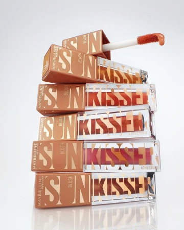Stack of Maybelline Sun-Kissed Blush product packaging, featuring blush compacts with applicator wands, bronze and clear containers, studio lighting.