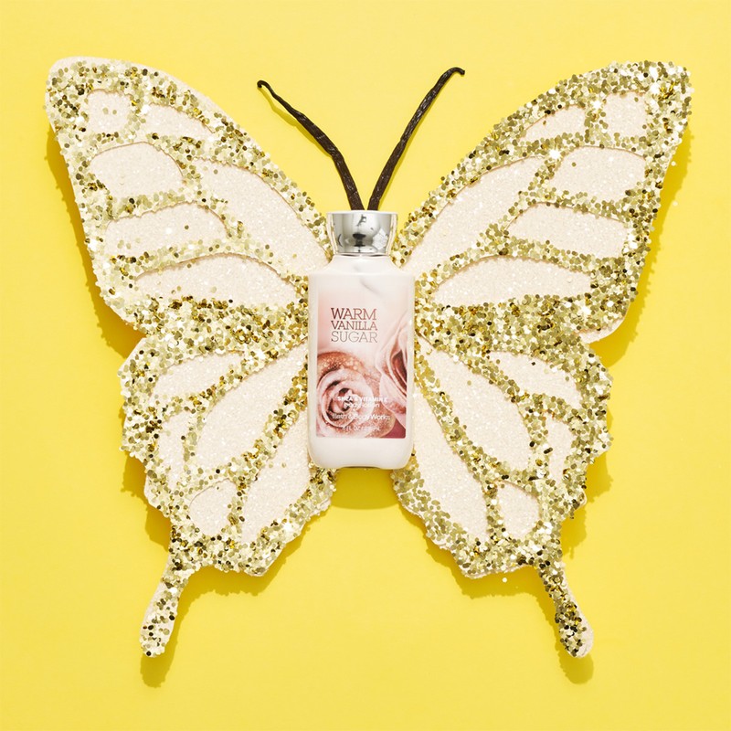 Bath & Body Works Warm Vanilla Sugar lotion bottle on a gold glitter butterfly against a bright yellow background in a studio setting.