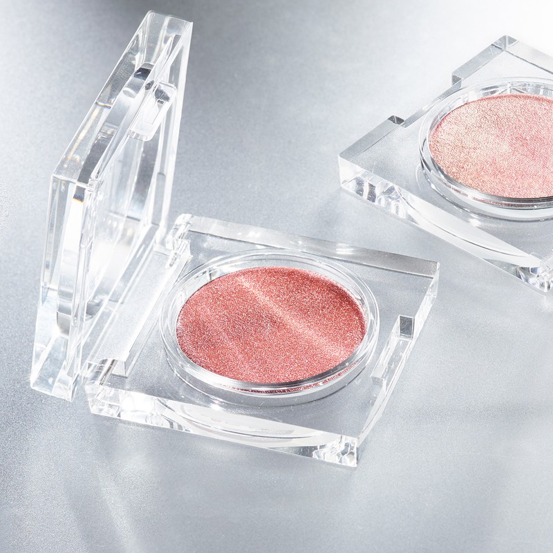 Close-up studio shot of transparent beauty compacts filled with shimmering pink powder against a silver surface. Beauty product.