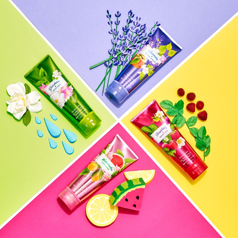Four Bath & Body Works lotion tubes arranged on a diagonally split background, showcasing floral and fruit themes in a vibrant, flat lay.