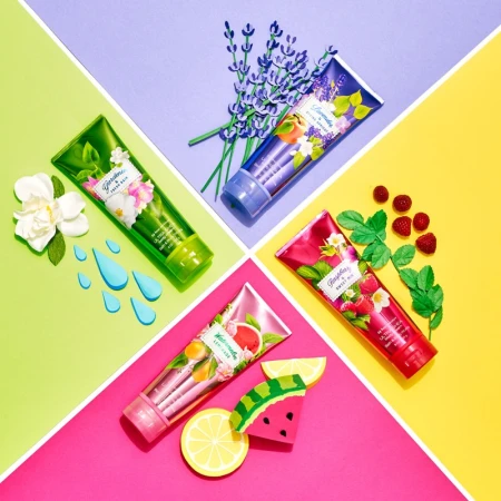 Four Bath & Body Works lotion tubes arranged on a diagonally split background, showcasing floral and fruit themes in a vibrant, flat lay.