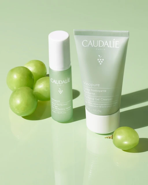 Studio shot of Caudalie Vinopure skincare products including a gel cleanser, serum, and green grapes, on a light green surface.