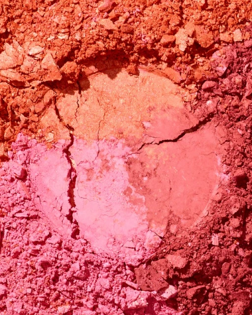 Close-up of cracked, colorful powder makeup in shades of pink, coral, and peach, filling the frame for beauty product display.