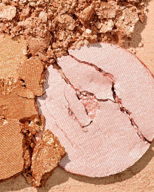 Close-up of a shattered, light-pink makeup powder compact, with an adjacent section of crushed bronze cosmetic powder.
