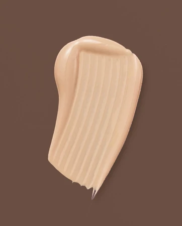 Close-up of light tan makeup foundation smear on brown background, showing its creamy texture and smooth appearance.