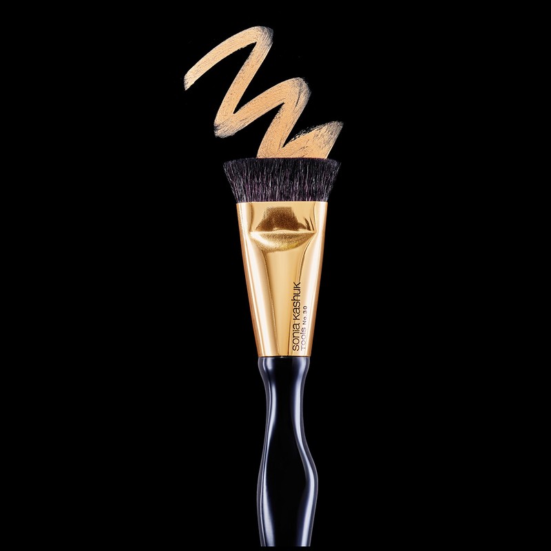 Cosmetic brush on black background with pale foundation makeup, beauty product flat lay. Elegant gold and black makeup brush.