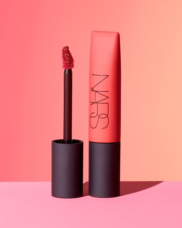 NARS brand red liquid lipstick on a pink surface against a gradient background. A beauty and cosmetics promotional studio shot.