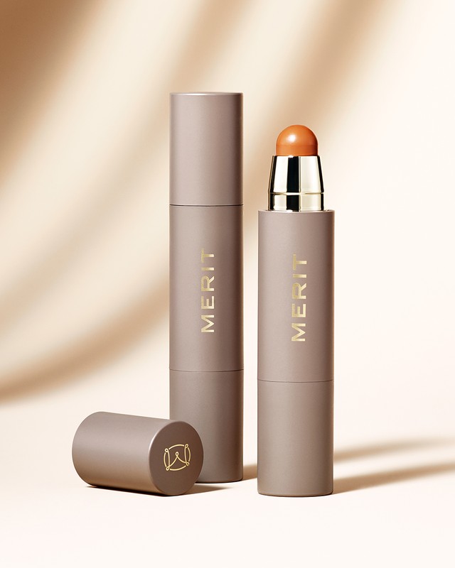 Merit Beauty: Beige cosmetic makeup sticks with branding on light gradient background, product photography for the beauty industry.