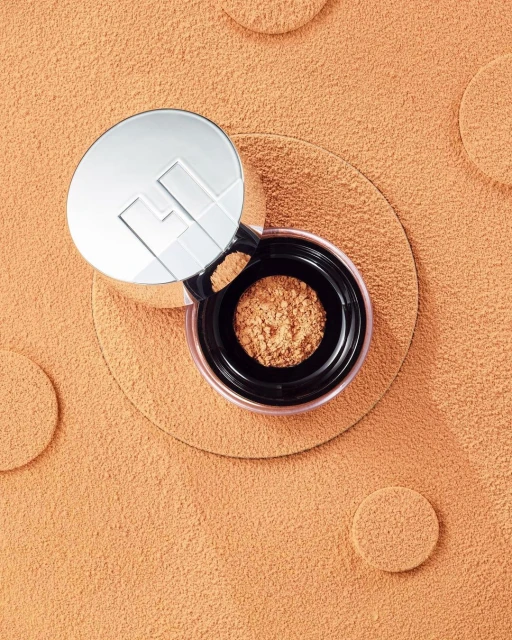 Top-down view of makeup compact on textured peach-colored surface with scattered circular peach shapes, studio shot.